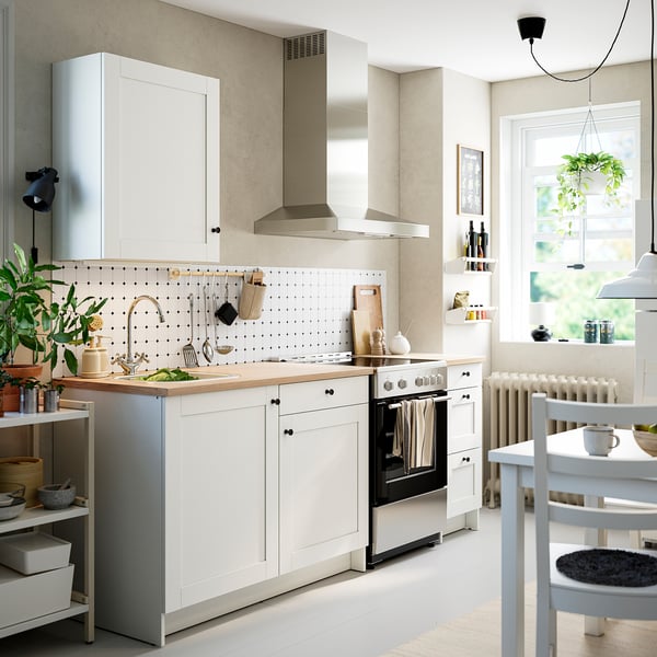 Small, modern kitchen with white cabinets. Stainless steel appliances and wood countertop. Plants add greenery near the window.