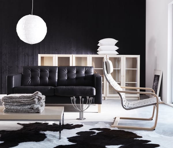 Modern living room: black leather sofa, white shelving, hide rug, hanging lamp.