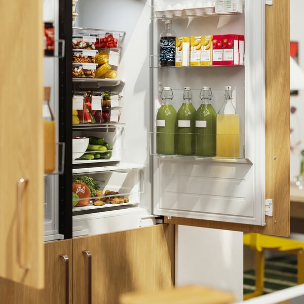 Open refrigerator showcasing KORKEN jars, storing liquids, fruit, and vegetables in organised shelves.