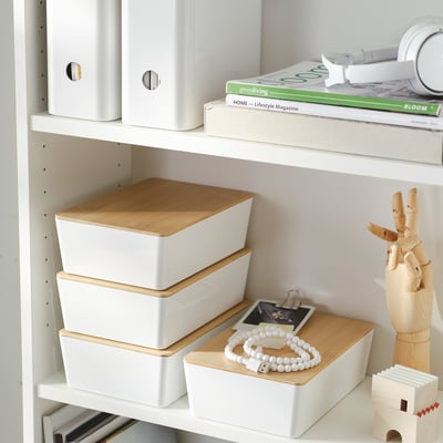 Bookshelf with white and wooden storage boxes, magazines, and a wooden hand figure.