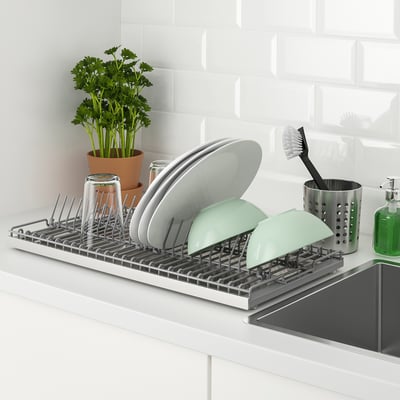 Kitchen dish drainer on counter stores washed items. Holds plates, cups, and cutlery, with a removable tray for collecting water.