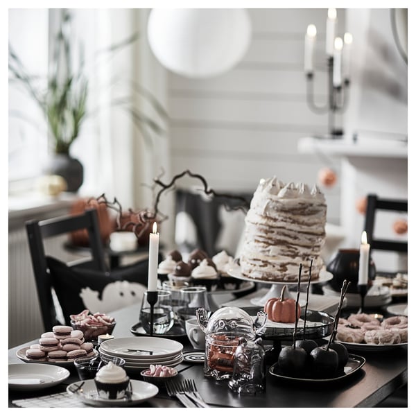 KUSTFYR black plates with spooky halloween decors, tiered cake with candles, desserts, and black chairs.