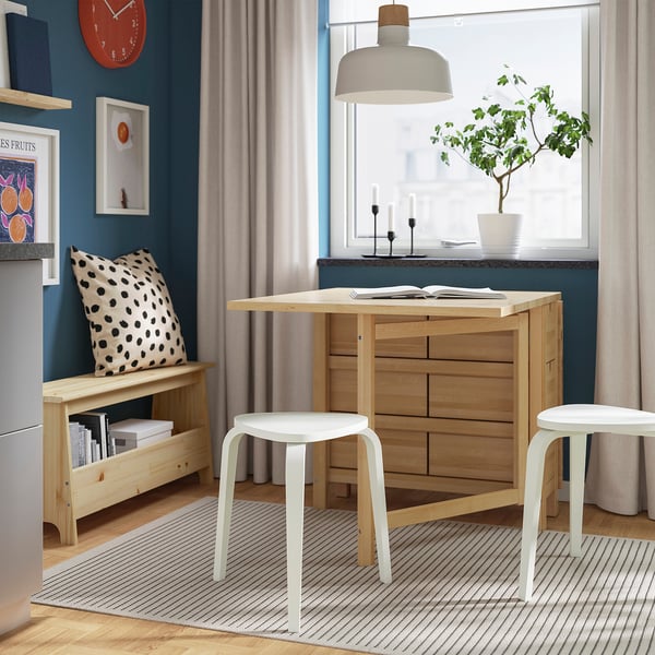 Stylish dining nook with KYRRE stool, wooden table, and bench. Blue-green walls, clock, and decor create warm, inviting atmosphere.