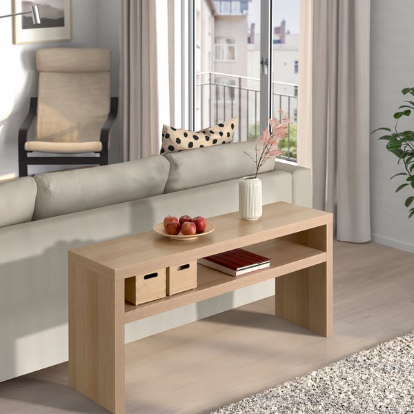 Living room with LACK table, apples, book, and vase. Beige sofa with pillows, large windows showing balcony.