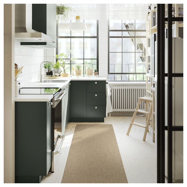 Modern kitchen with green cabinets, large window, wooden stools, and a beige LÄTTBETONG rug.