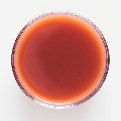 Clear glass filled with reddish-pink smoothie, likely made from mixed berries and apples, with a straw for drinking.