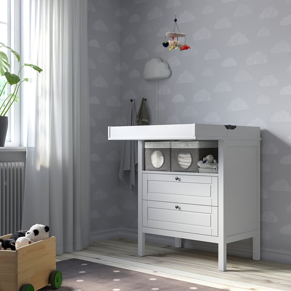 Nursery changing station with cloud wallpaper, storage box, bassinet, toys.