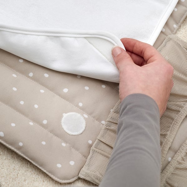 Person placing babycare mat with white polka dots and mesh pocket.