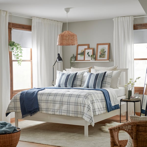 Bedroom with white LINSNÄRJA comforter, blue accents, wooden frames, hanging plants, and a wicker chair.