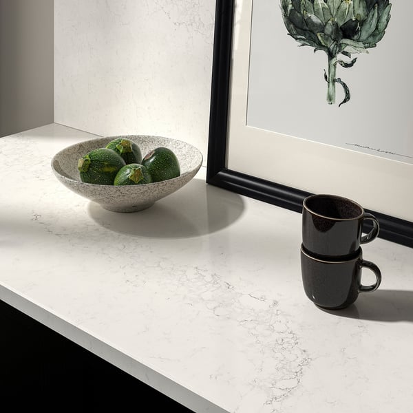 White marble countertop with speckled bowl of limes and dark mugs. Beside framed art.