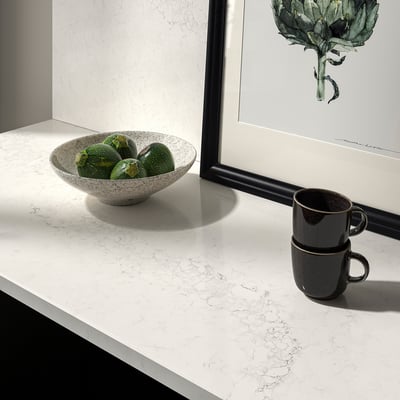 White marble countertop with speckled bowl of limes and dark mugs. Beside framed art.