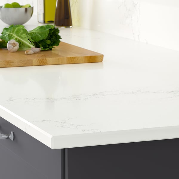 Modern kitchen counter with fresh produce; white worktop, grey cabinets; functional, stain-resist.