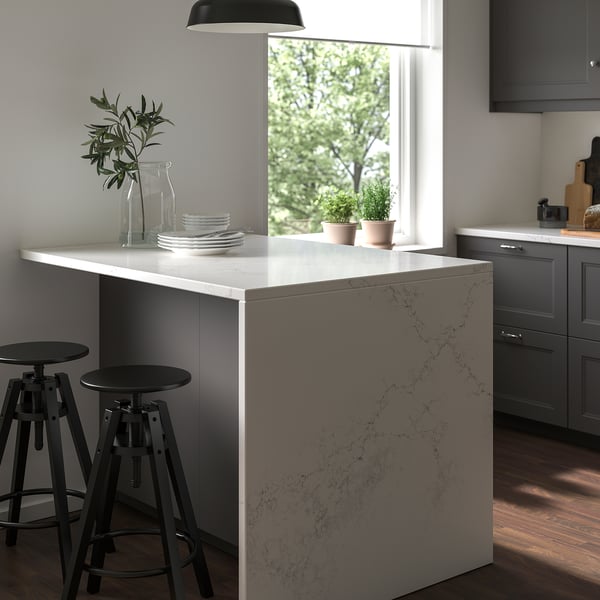 Modern kitchen with white LOCKEBO quartz island, black stools, grey cabinets, and plants.