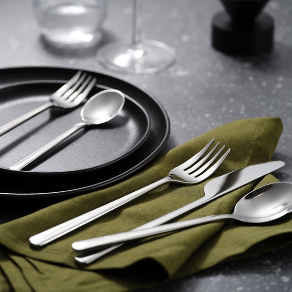 Modern table setting: black plates, silver cutlery, olive napkins, wine glasses.