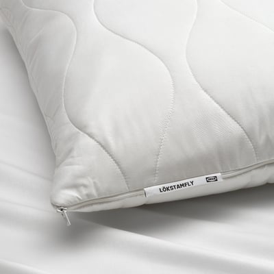 Close-up of a white, ergonomic LÖKSTAMFLY pillow with textured surface, zip, and label.