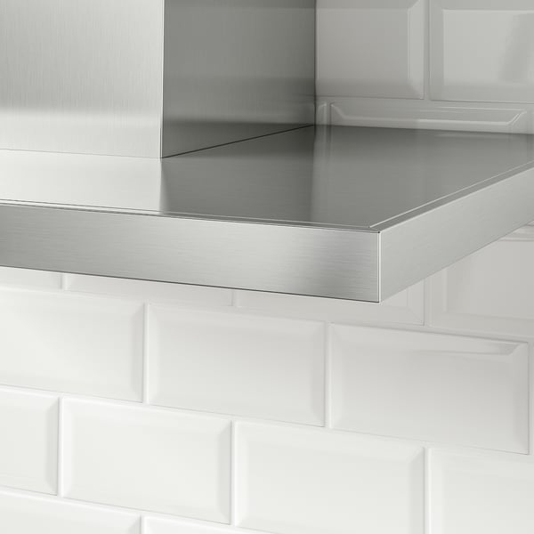Stainless steel kitchen hood with sleek design, reflecting light, mounted against white tiled wall.