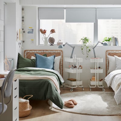 Two beds with green waffle comforters, lamps, plants, and large window.