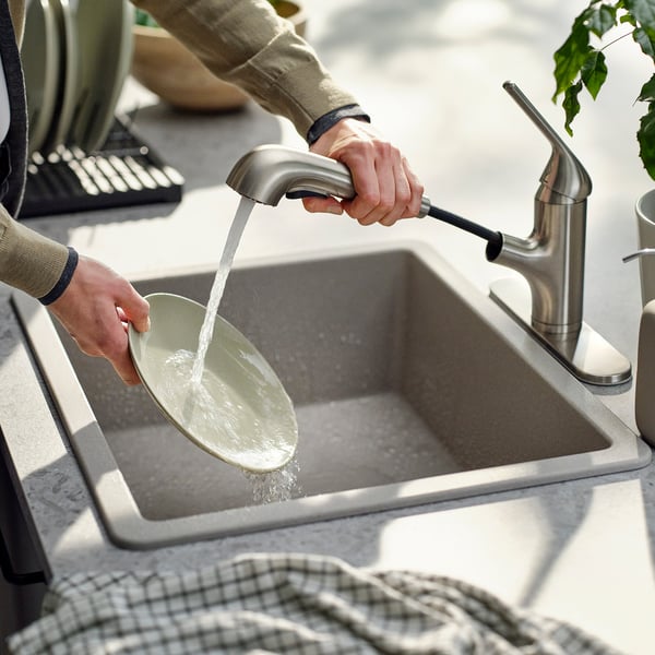 Person washing dish under MACKSJÖN tap, using spray head function.