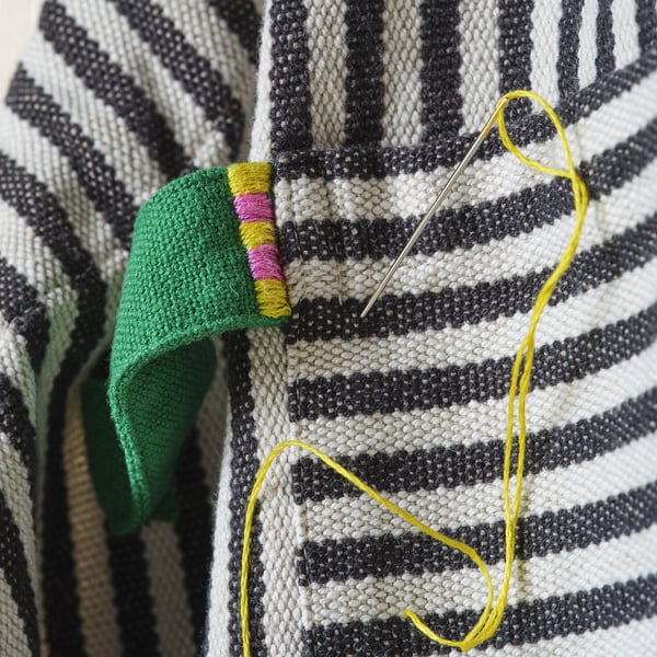 Close-up of black and white striped knit apron with green strap, yellow thread, and needle; showcasing detailed craftsmanship.