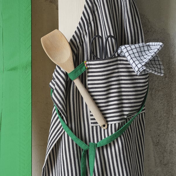 A striped apron with a green strap holds cooking tools. The apron has pockets, perfect for kitchen use.