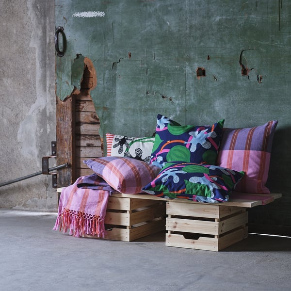 Colourful cushions on wooden crates, hand-embroidered, against a distressed wall.