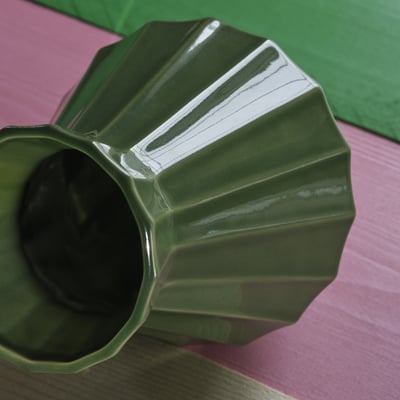 Handcrafted green stoneware vase with sharp geometric edges, resting on a pink tablecloth.