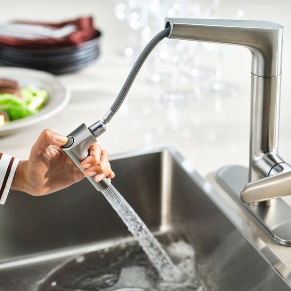 Person operates modern kitchen tap with pull-out spray head, providing versatile water flow options.