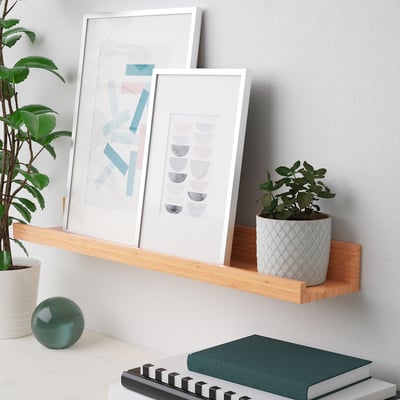 Minimalist wall shelf displays framed art and plants. Groove holds frames securely.