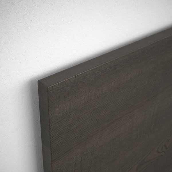 Close-up of dark wooden headboard, smooth finish against white wall.