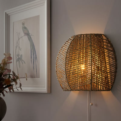 Wall-mounted MÅNALG lamp, hand-braided sedge shade emits warm, decorative light.