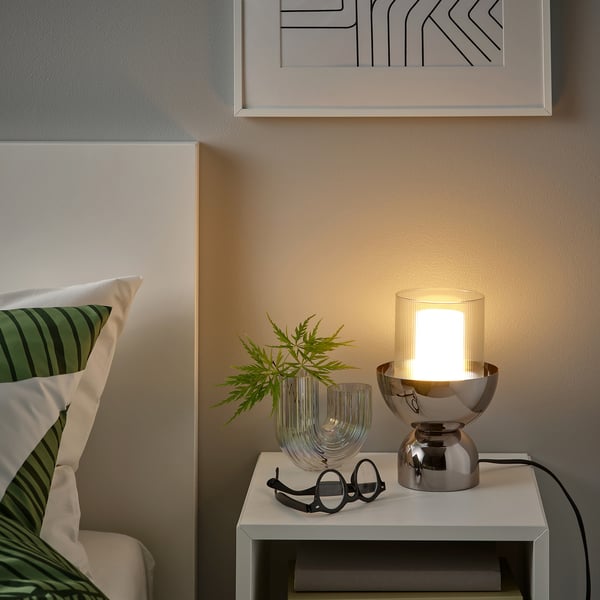 Cosy bedroom nook with green pillows and modern MOLNART lamp.