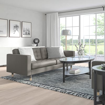 Modern living room with a grey MORABO sofa, circular glass coffee table, and large window. Black and white decor with natural light.