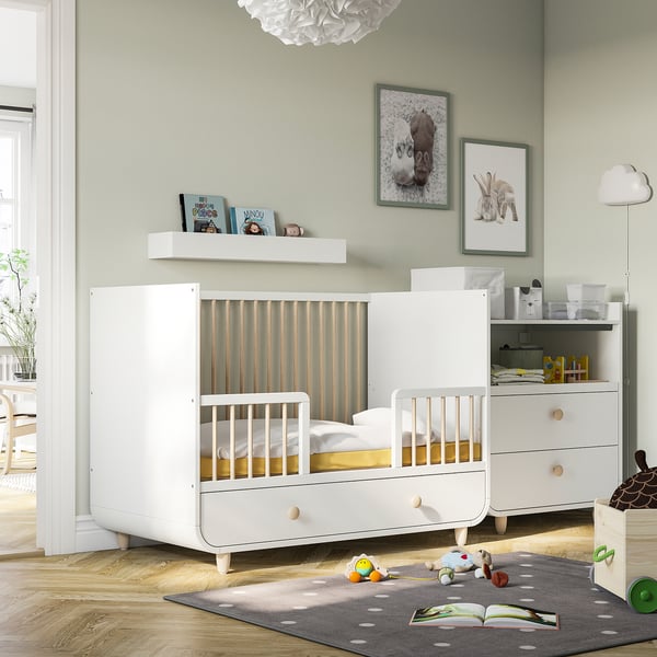 Green nursery with white MYLLRA cot, adjustable base, bookshelves, dresser and toys.