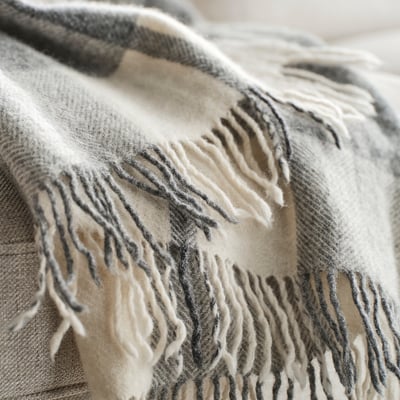 Cosy grey throw blanket with fringe, soft wool texture, handwoven check pattern, inviting warmth and comfort.
