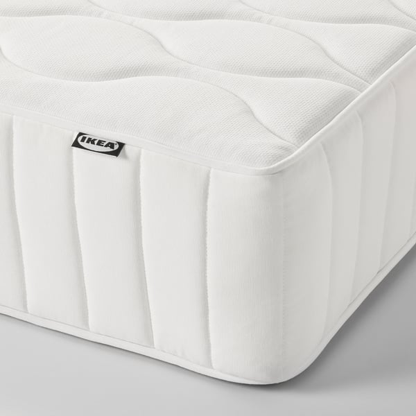 Close-up of a modern, white mattress with an IKEA tag, featuring a wave-patterned surface and vertical stitching, suggesting high quality and comfort.