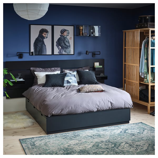 Modern bedroom with dark blue walls, grey bedding, and wooden wardrobe; two art frames above the bed.