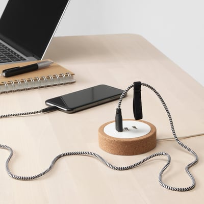 A minimalist desk setup featuring a black smartphone charging via a stylish cork-based usb charger with multiple ports.