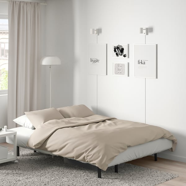 Minimalist bedroom with NYHAMN bed, beige blanket, white lamps, art prints. Bed is centred, large, flanked by small tables, lamps taller.