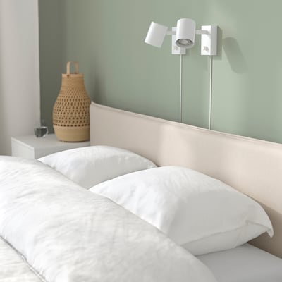 Cosy bedroom with dimmable wall lights for reading, featuring a woven vase and cup on the side table.