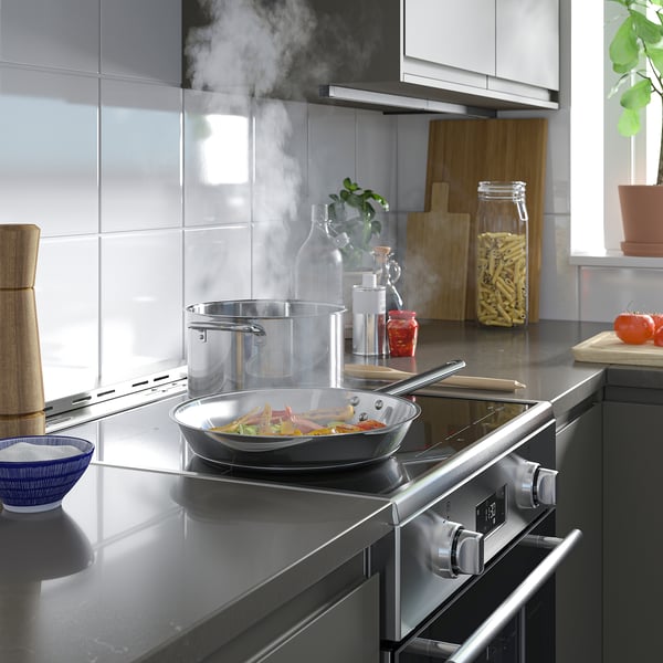 Kitchen counter with black stove, pots, knife, plants, tomatoes, steam rising