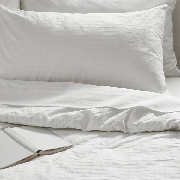 White bedding with striped pillow sham, smoothly textured duvet, and open book on crisp, breathable cotton.
