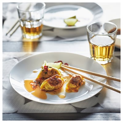 White glass dish with dumplings, sauce, and chopsticks beside two glasses of drink.