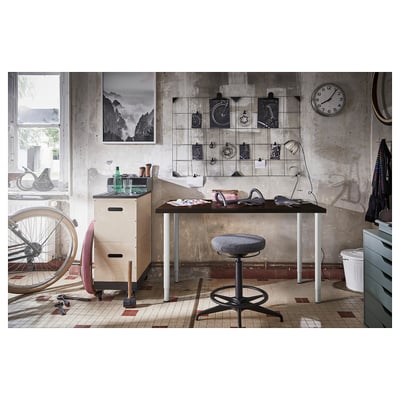 Industrial office setup with OLOV adjustable black desk, contrasting white legs, featuring a chair, bicycle, and wall decorations in a rustic room.