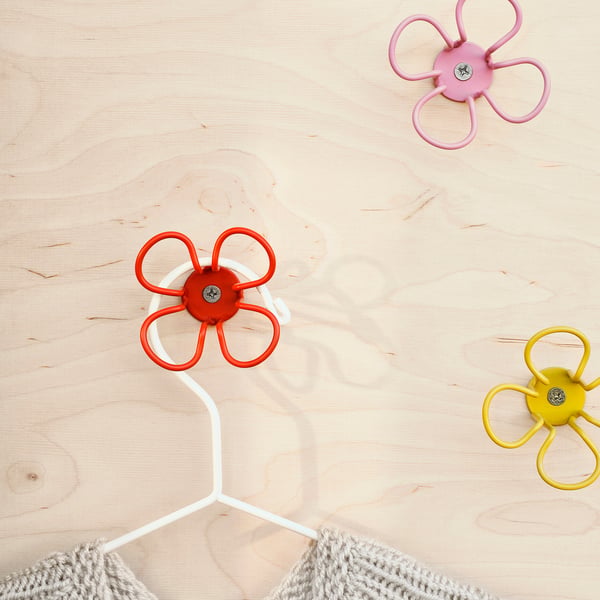 Three colourful flower-shaped wall hooks on a wooden surface, one holding a white cable.