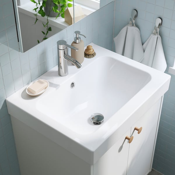 Modern bathroom sink with chrome tap, soap dispenser, and towel hooks. A deep ceramic basin prevents water spills on the floor.