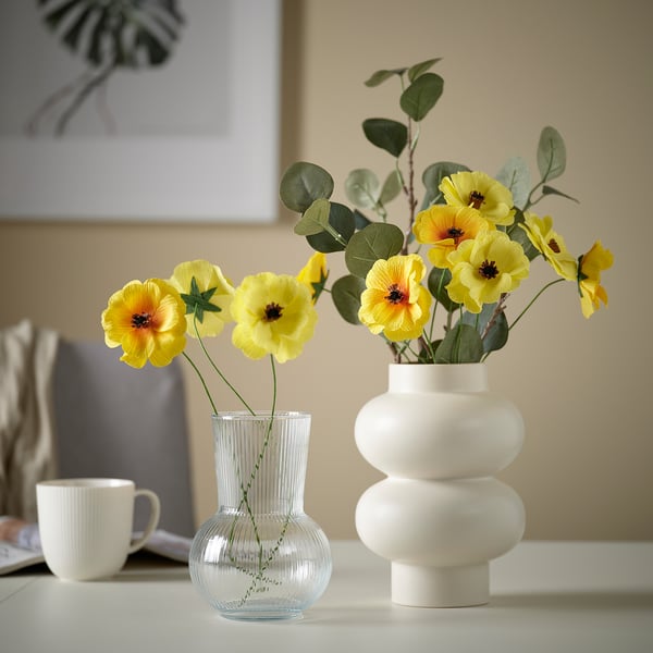 Two vases with yellow flowers: one small, ribbed glass, the other large, white ceramic.
