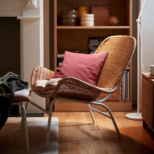 Cosy living room with wicker chair PARADISBUSKE in tan, featuring red pillow, placed by wooden bookshelf.