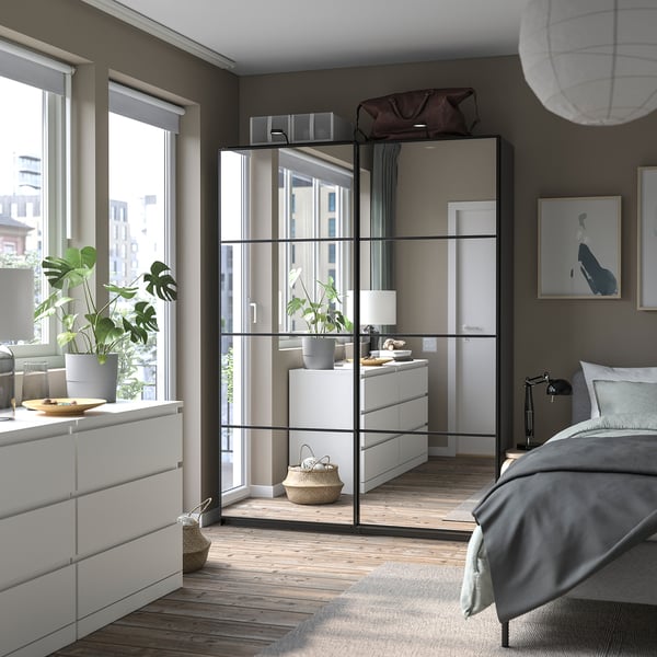 Modern bedroom with glass-fronted PAX wardrobe, potted plants, and a bed with grey bedding.
