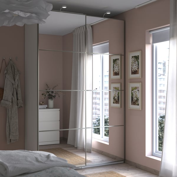 Modern bedroom with large mirror wardrobe, white bedding, grey curtains, and floral pictures on beige walls.