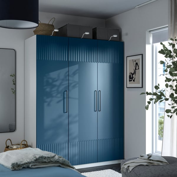 Modern bedroom with blue PAX wardrobe, mirror, and plant decor. Grey bed partly visible.